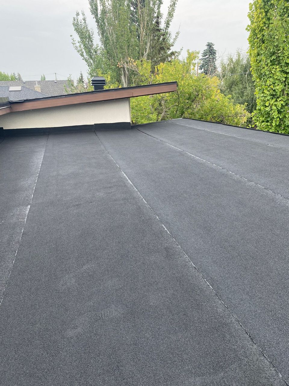 New granulated SBS cap sheet on a lower flat roof against a stucco wall