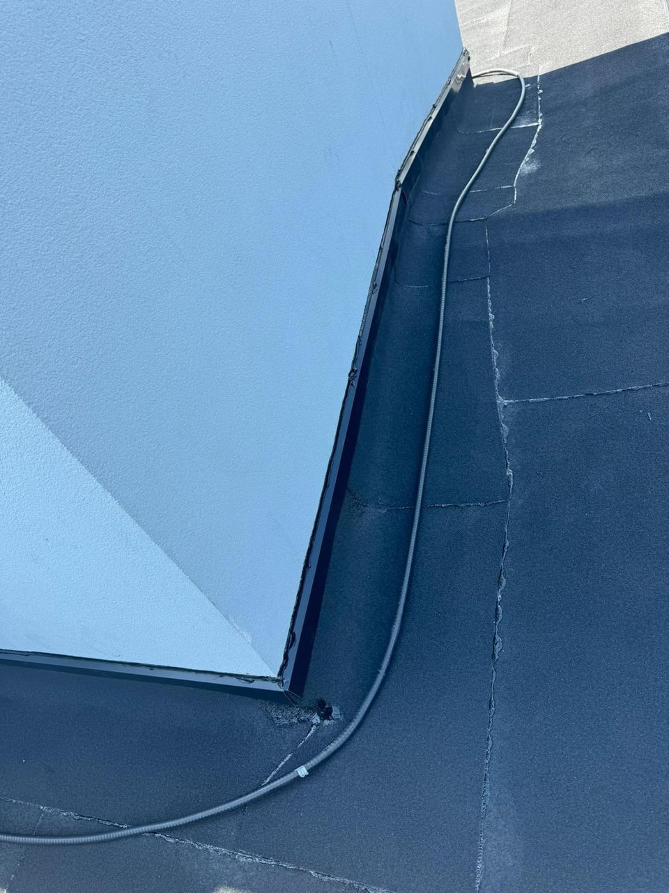 Open seams on an aged flat roof membrane running along a stucco wall